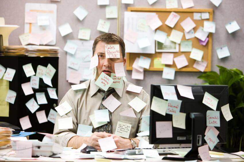 Overwhelmed man at desk covered in sticky notes illustrating inefficient client management processes.