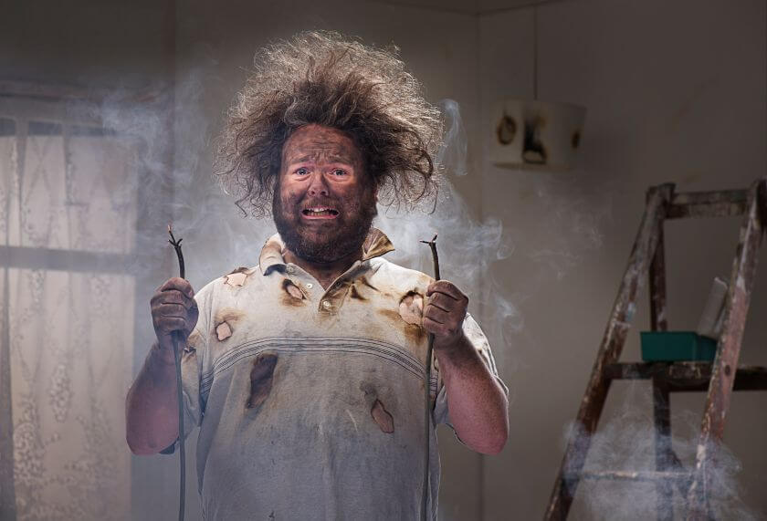 Man with shocked expression holding damaged electrical wires, illustrating potential disaster in custom application development.